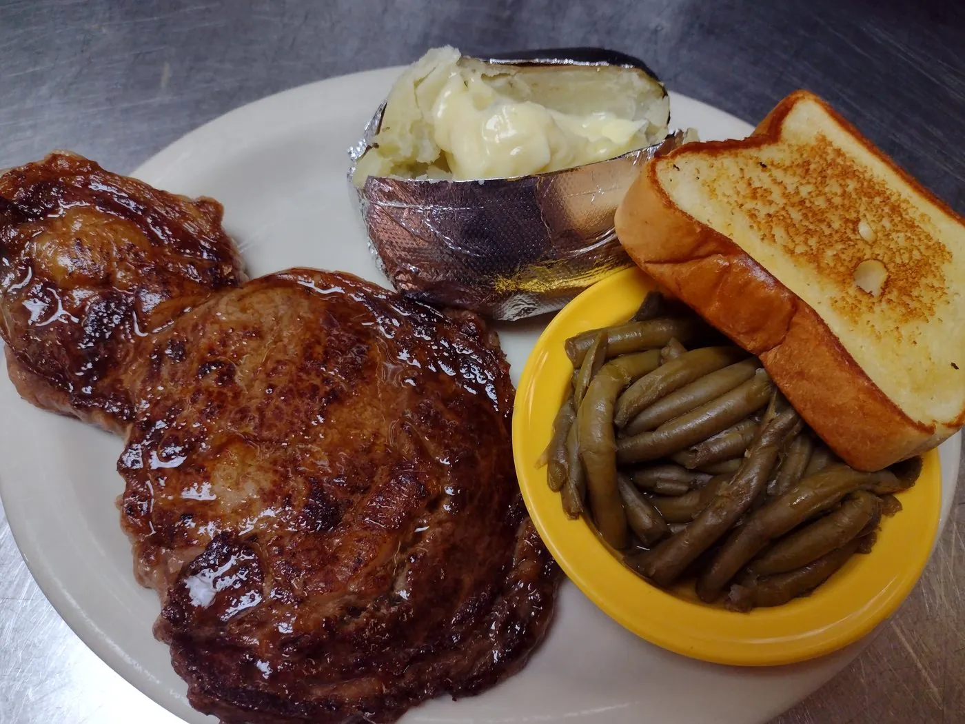 Hand-cut ribeye steak with baked potato, green beans, and Texas toast
